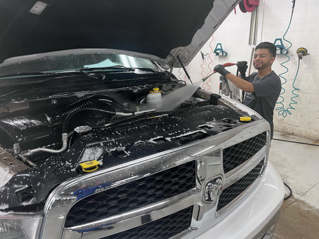 Crystal Clean employee cleaning the engine of a Dodge truck