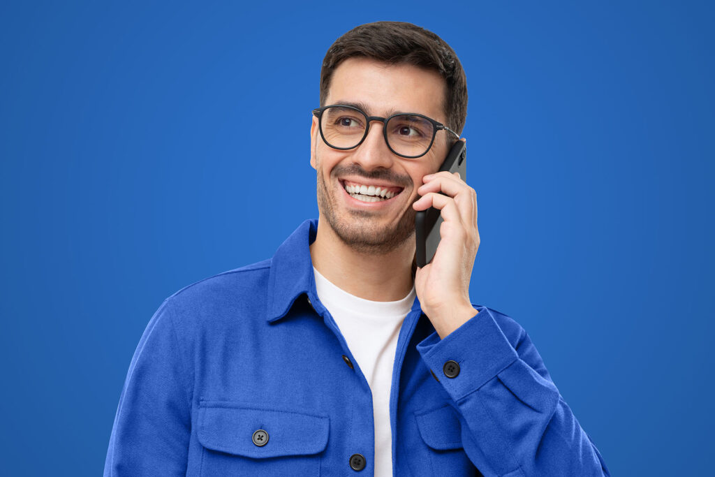 Young man in blue shirt and glasses talking on the phone, isolated on blue